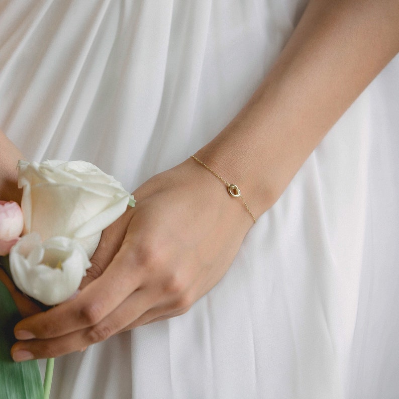 May include: A delicate gold chain bracelet with a small, circular pendant. The bracelet is worn on a person's wrist.