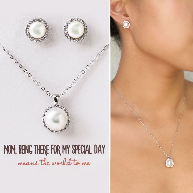 Puede incluir: Un conjunto de collar y aretes de plata con un dije de perla y aretes de bot&oacute;n de perla a juego. El dije y los aretes est&aacute;n rodeados por un halo de peque&ntilde;as piedras transparentes. El collar tiene una cadena delicada. La imagen incluye el texto "MOM, BEING THERE FOR MY SPECIAL DAY means the world to me".