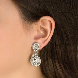 May include: A pair of silver teardrop earrings with clear crystal stones. The earrings have a double teardrop design with smaller stones surrounding the larger stones.