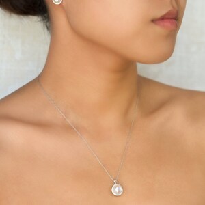 Puede incluir: Un collar de plata con un colgante de perla rodeado de peque&ntilde;os diamantes. El colgante es redondo y cuelga de una cadena delicada. El collar lo lleva una persona de piel clara.