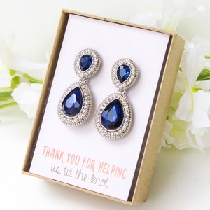 May include: A pair of blue teardrop earrings with a smaller teardrop stone above the larger one. The earrings are in a small box with the text "Thank you for helping us tie the knot".