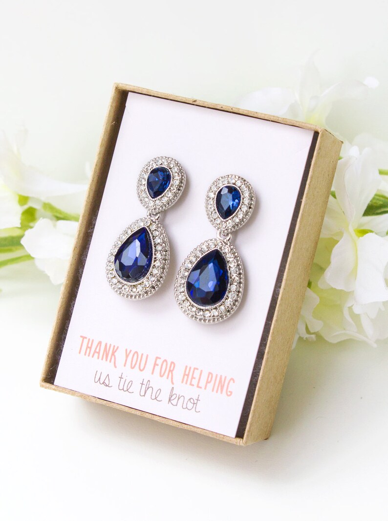 May include: A pair of blue teardrop earrings with a smaller teardrop stone above the larger one. The earrings are in a small box with the text "Thank you for helping us tie the knot".