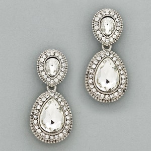 May include: A pair of silver teardrop earrings with clear crystal accents. Each earring features two teardrop-shaped crystals, one smaller than the other, surrounded by a halo of smaller crystals.