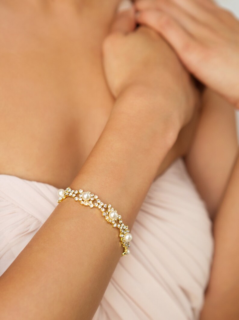 May include: A gold bracelet with a delicate design featuring small pearls and rhinestones.