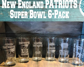 Könnte beinhalten: Sechs klare Glasbierkrüge mit geätzten Designs der Super Bowl-Siege der New England Patriots. Die Krüge sind auf einer Holzoberfläche angeordnet. Der Text "NEW ENGLAND PATRIOTS SUPER BOWL 6-PACK" befindet sich oben im Bild. Der Text "FREE SHIPPING" befindet sich unten im Bild.