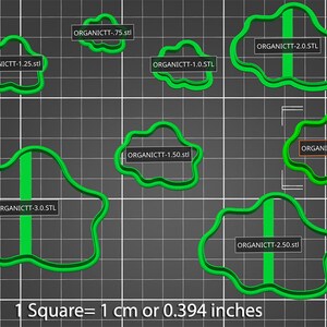 May include: A set of seven green plastic cookie cutters in various sizes, ranging from 0.75 inches to 3 inches in diameter. The cutters are shaped like irregular organic shapes with a vertical line down the center. The image includes a scale showing that one square equals 1 centimeter or 0.394 inches.