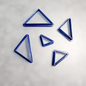Pode incluir: Cinco cortadores de biscoitos de plástico azul em forma de triângulo de diferentes tamanhos.
