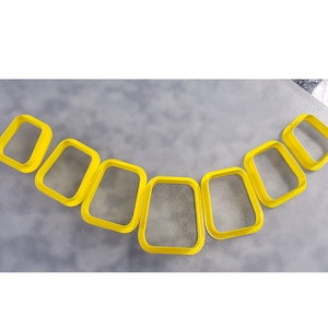 Puede incluir: Un juego de ocho cortadores de galletas de plástico amarillo en forma de rectángulos, dispuestos en semicírculo.