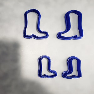 May include: Four blue plastic cookie cutters shaped like cowboy boots. The cutters are in two sizes, with two of each size.