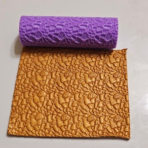 May include: A purple rolling pin with a mushroom pattern, used to create an embossed design on a gold sheet of fondant.