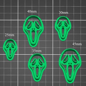 May include: Five green plastic cookie cutters shaped like a screaming face. The cutters are arranged in a grid pattern on a green grid background. The cutters are labeled with their size in millimeters: 25mm, 30mm, 35mm, 40mm, and 45mm.