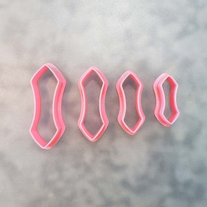 May include: Four pink plastic cookie cutters shaped like a pointed oval. The cutters are different sizes, with the largest cutter on the left and the smallest cutter on the right.