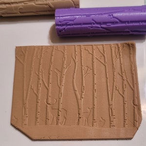 May include: A brown clay tile with an embossed design of a forest scene with trees and deer. The tile is textured and has a rustic look.