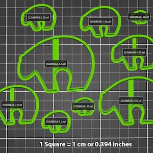 May include: A set of ten green plastic bear cookie cutters in various sizes. The cutters are arranged on a black and white grid background. The text "1 Square = 1 cm or 0.394 inches" is printed below the cutters.