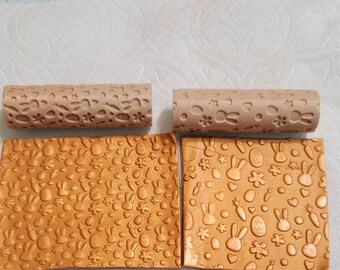 Könnte beinhalten: Zwei braune Nudelhölzer mit einem sich wiederholenden Muster aus Hasen, Eiern, Karotten und Blumen. Die Nudelhölzer liegen neben zwei Blättern goldfarbenem Fondant mit dem gleichen Muster, das in die Oberfläche geprägt ist.