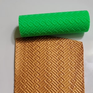 May include: A green silicone rolling pin with a geometric pattern. The rolling pin is used to create a textured design on fondant or other edible materials.