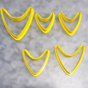 May include: Five yellow plastic cookie cutters shaped like a retro mid-century modern atomic age design. The cutters are in various sizes.