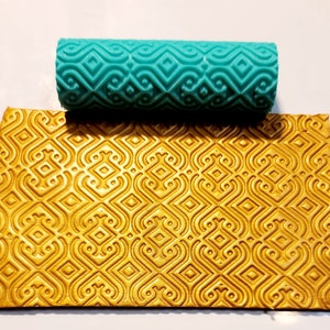 May include: A turquoise rolling pin with a geometric pattern is shown next to a sheet of gold fondant with the same pattern embossed into it.