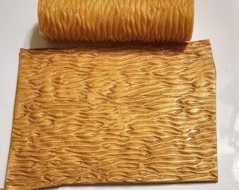 May include: A brown rubber roller with a wavy texture, used for creating a wood grain effect on fondant or other edible materials. The roller is shown next to a piece of fondant with the wood grain pattern.