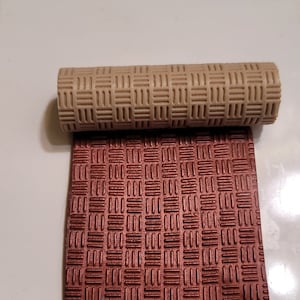 May include: A close-up of two textured rolling pins. The top rolling pin is beige and the bottom rolling pin is a deep reddish-brown.