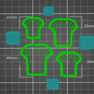 May include: Four green plastic cookie cutters shaped like t-shirts with a spiderweb design. The cutters are on a black and white grid background. The cutters measure 25mm, 30mm, 35mm, and 40mm.