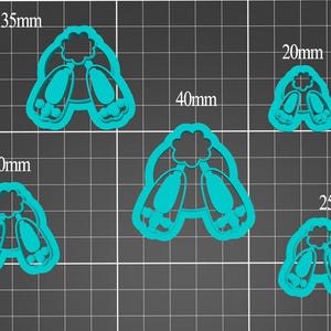 May include: A collection of five teal-colored cookie cutters in the shape of ballet slippers. Sizes range from 0.79 inches to 1.57 inches in width. The cutters are displayed on a dark gray grid background.