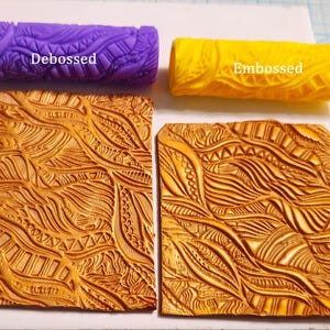 May include: A purple debossed and yellow embossed clay roller with intricate patterns, alongside two golden-brown clay tiles with matching designs. The text "Debossed" and "Embossed" are visible on the rollers. The tools are used for crafting.