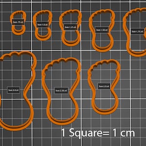 May include: A set of ten orange plastic cookie cutters shaped like feet in various sizes, ranging from 0.75 inches to 3 inches. The cutters are arranged on a black and white grid background. The text "1 Square = 1 cm" is printed below the cutters.