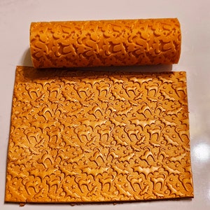 May include: A gold-colored rolling pin with a repeating pattern of bats and cats. The rolling pin is used to create an embossed design on fondant or dough.