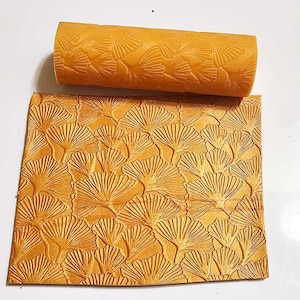 Puede incluir: Un rodillo dorado con un patrón de hojas de ginkgo. El rodillo se utiliza para crear un diseño en relieve en fondant o masa.