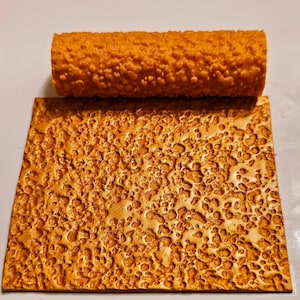 May include: A close-up of a textured rubber roller with a bumpy surface. The roller is orange and has been used to create a textured pattern on a surface.