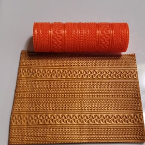 May include: A close-up of a red rolling pin with a decorative pattern. The rolling pin is used to create an embossed design on a gold surface.