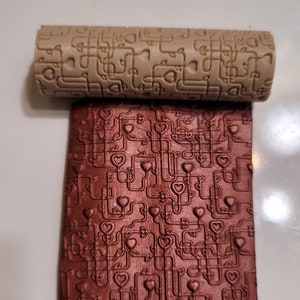 May include: A brown rolling pin with a repeating pattern of hearts and leaves. The rolling pin is used to create an embossed pattern on a red surface.