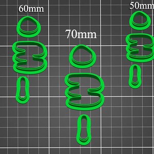 Puede incluir: Conjunto de cinco cortadores de galletas de plástico verde de diferentes tamaños. Los cortadores tienen forma de óvalo simple, forma de doble bucle y bucle simple. Los cortadores están dispuestos en filas sobre un fondo de cuadrícula verde. Las medidas de los cortadores están etiquetadas en milímetros.