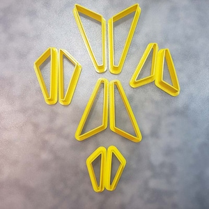 May include: A set of nine yellow plastic cookie cutters shaped like triangles. The cutters are arranged in a symmetrical pattern.