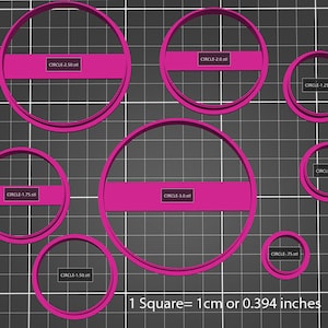 Puede incluir: Un conjunto de nueve cortadores de galletas de plástico rosa en varios tamaños de círculo, que van desde 1,25 cm hasta 7,5 cm de diámetro. Los cortadores están dispuestos sobre un fondo de cuadrícula negra. El texto "1 Cuadrado = 1 cm o 0,394 pulgadas" está impreso debajo de los cortadores.
