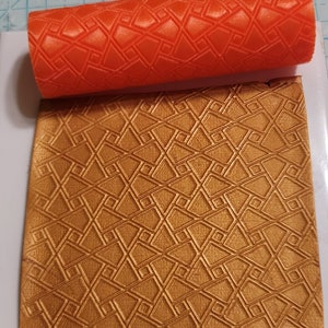 May include: A close-up of a bright orange rolling pin with a geometric pattern. The rolling pin is used to create an embossed pattern on a sheet of gold-coloured fondant.