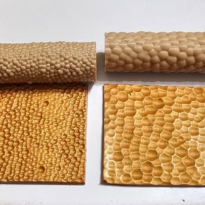 Könnte beinhalten: Zwei strukturierte Nudelrollen und zwei quadratische, strukturierte Fliesen. Die Nudelrollen und Fliesen haben ein sich wiederholendes Muster aus abgerundeten, erhabenen Noppen. Die Artikel sind in Beige- und Goldtönen gehalten und auf einer weißen Oberfläche angeordnet.