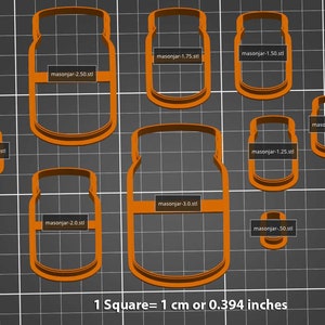 May include: A set of nine orange plastic cookie cutters shaped like mason jars in various sizes. The cutters are arranged on a grey grid background. The text "1 Square = 1 cm or 0.394 inches" is printed below the cutters.