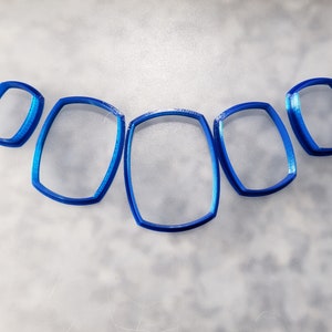 May include: Five blue plastic cookie cutters in different sizes, shaped like rounded rectangles.