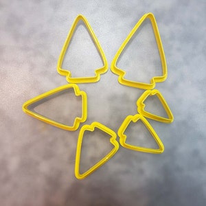 May include: Six yellow plastic cookie cutters shaped like arrowheads. The cutters are arranged in a star shape.