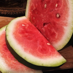Peut inclure: Gros plan sur une pastèque coupée en tranches sur une planche à découper en bois. La pastèque est rouge et juteuse avec des graines noires.