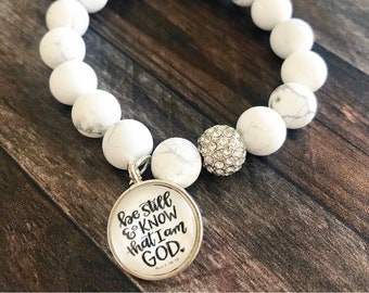 May include: White beaded bracelet with a silver charm that says "Be still & know that I am GOD". The charm is attached to a silver bead with rhinestones.