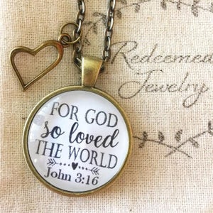 May include: A gold necklace with a heart charm and a round pendant with the text "For God so loved the world John 3:16".