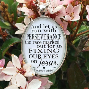 May include: White oval pendant necklace with a black and white inspirational quote: "And let us run with perseverance the race marked out for us, fixing our eyes on Jesus."  The quote is from Hebrews 12:1-2.