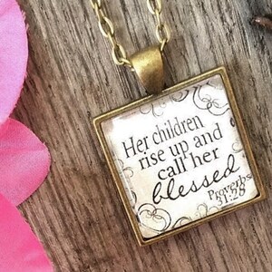 May include: A gold necklace with a square pendant featuring the quote "Her children rise up and call her blessed" with the scripture reference "Proverbs 31:28".