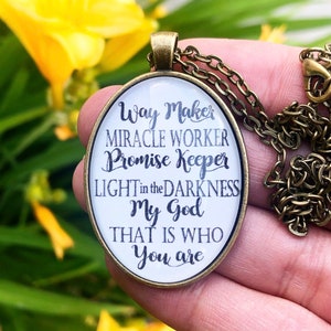 Könnte beinhalten: Eine goldfarbene Halskette mit einem ovalen Anhänger, auf dem der Text "Way Maker, Miracle Worker, Promise Keeper, Light in the Darkness, My God, That is Who You Are" steht.