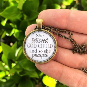 May include: A gold necklace with a round pendant featuring the text "She believed GOD COULD and so she prayed".