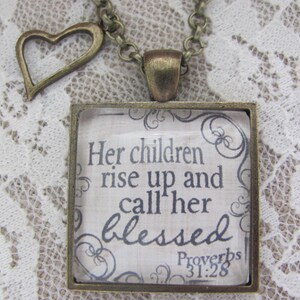 May include: A bronze necklace with a square pendant featuring the quote "Her children rise up and call her blessed" from Proverbs 31:28. The pendant has a heart-shaped charm attached to the chain.