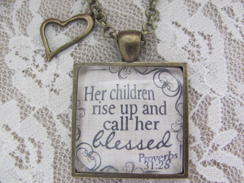 May include: A bronze necklace with a square pendant featuring the quote "Her children rise up and call her blessed" from Proverbs 31:28. The pendant has a heart-shaped charm attached to the chain.